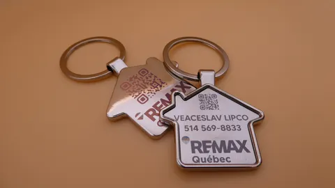Custom house-shaped metal keychains with laser-engraved RE/MAX branding, QR codes, and color marking. A personalized gift for real estate agents created by TechArt Concept.