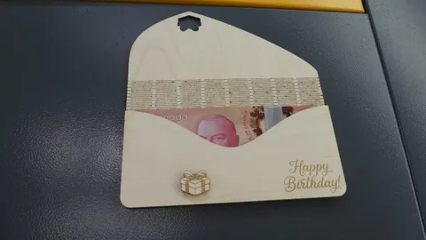 Open laser cut wooden birthday card holding a Canadian fifty dollar bill on a dark work surface.